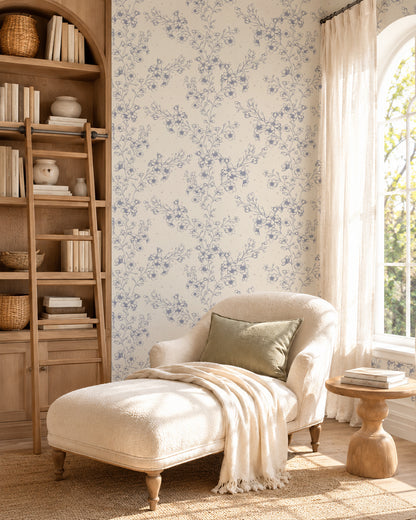 Blossom Whisper Periwinkle floral wallpaper in a cozy reading nook with a cream chaise, wooden shelving and soft natural light.