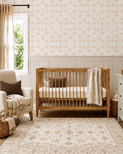 Boho Weave Clay wallpaper in a warm nursery with a wood crib, cream armchair and soft neutral accents.