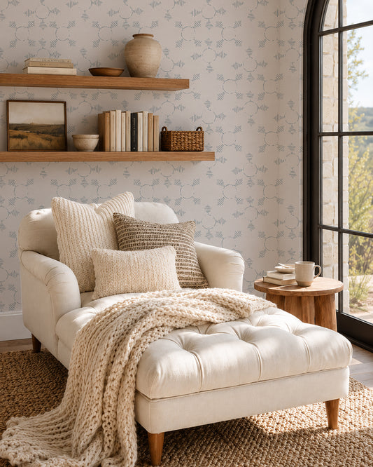 Boho Weave Dusty Blue wallpaper in a cozy reading nook with a cream chaise, wood shelves and soft natural light.