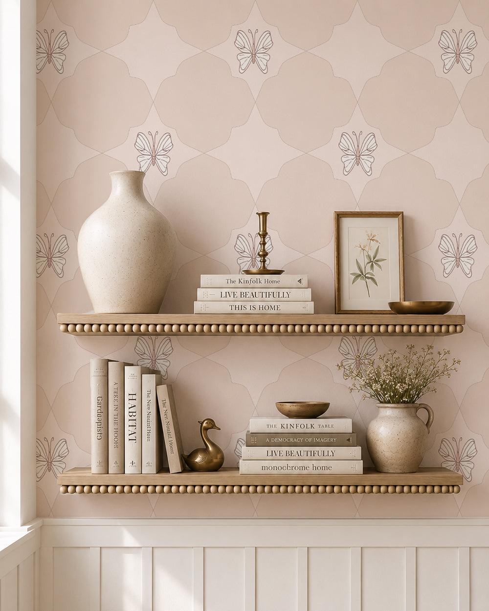 Keepsake Pale Blush wallpaper behind styled shelves with books, pottery and warm brass accents.