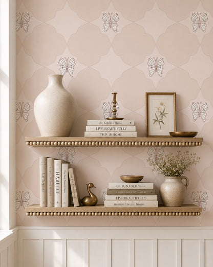 Keepsake Pale Blush wallpaper behind styled shelves with books, pottery and warm brass accents.