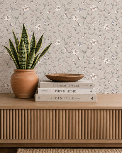 Magnolia Bloom Taupe wallpaper behind a wooden console styled with books, pottery and a potted plant.