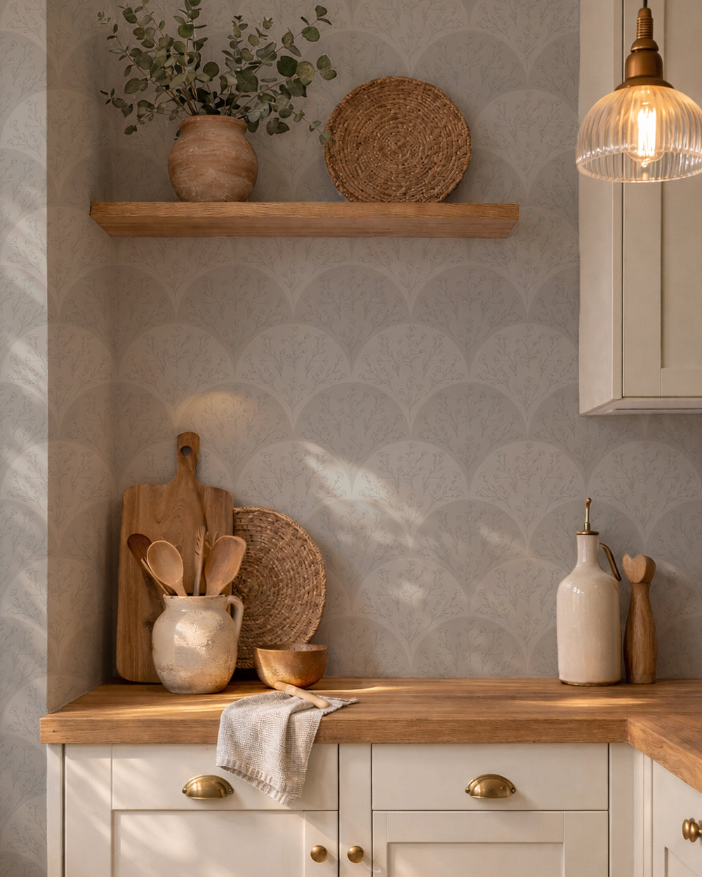 Soft sage floral fan wallpaper in a cozy kitchen with warm wood accents, pottery and open shelving.
