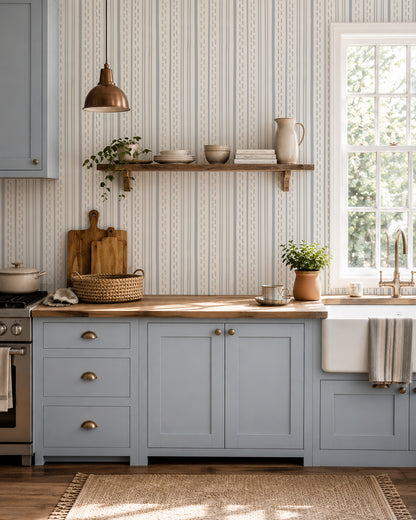 Ticking Stripe Dusty Blue on Cream wallpaper in a cozy kitchen with blue cabinets, wood counters and warm natural light.