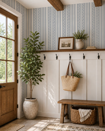 Ticking Stripe Dusty Blue wallpaper in a cozy entryway with white paneling, a wood bench and leafy plant.