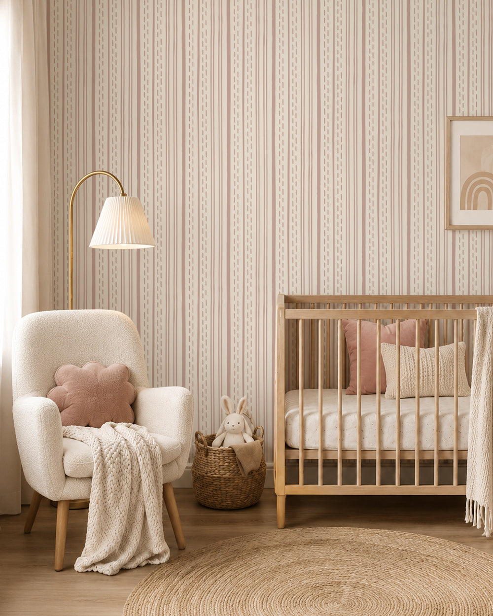 Ticking Stripe Soft Blush on Cream wallpaper in a cozy nursery with a wood crib, cream armchair and blush accents.