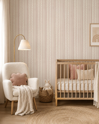Ticking Stripe Soft Blush on Cream wallpaper in a cozy nursery with a wood crib, cream armchair and blush accents.