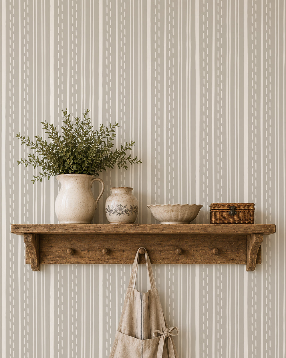 Ticking Stripe Soft Taupe wallpaper behind a rustic wood shelf with cream pottery and leafy greenery.